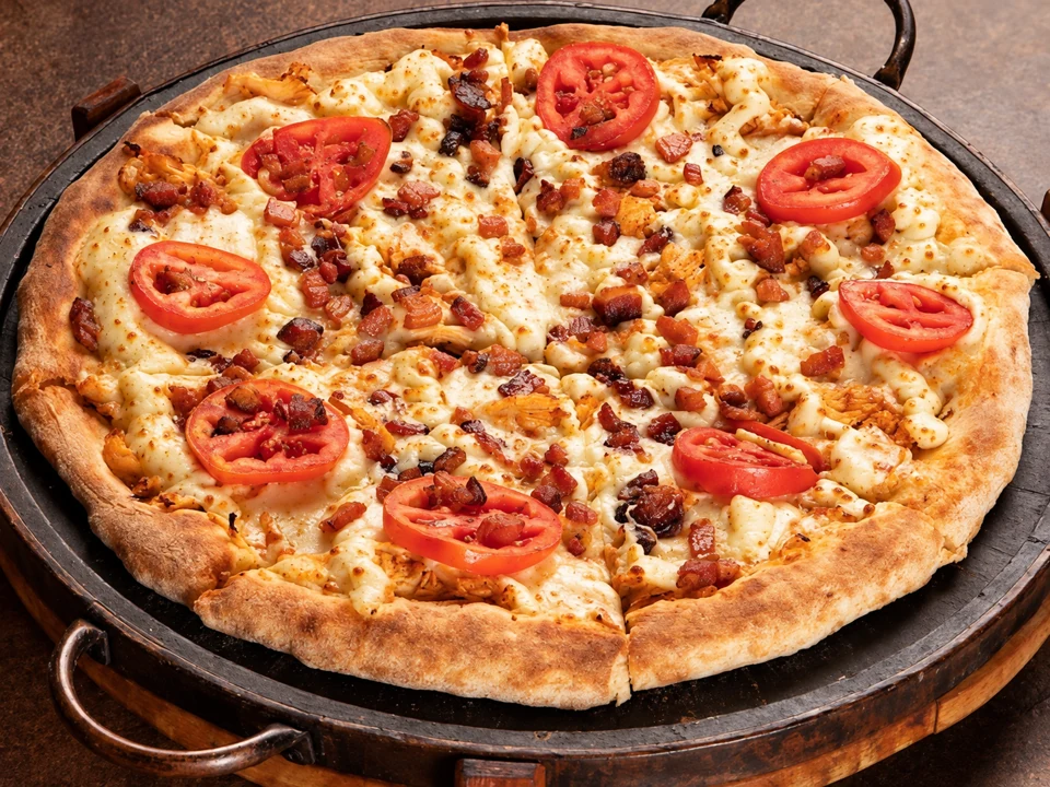 Pizza com queijo, tomate e bacon em assadeira redonda escura com alças