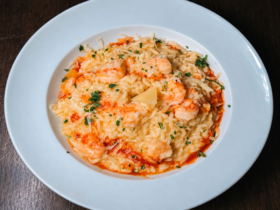 Risoto cremoso de camarão com parmesão em prato redondo claro sobre mesa de madeira
